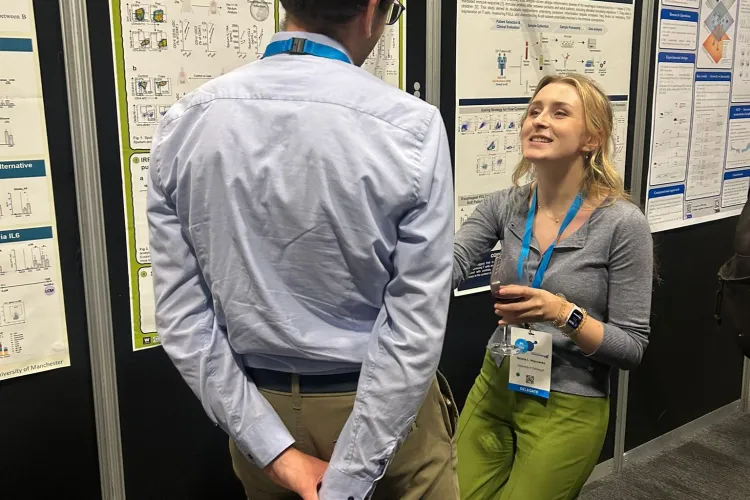 Photograph showing two people engaged in discussion at a scientific conference poster session, with multiple research posters displayed.