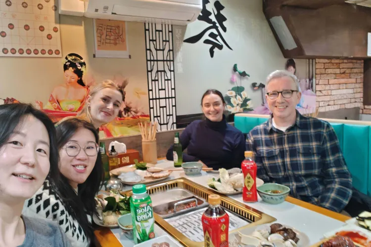 A group dining around a grill table with assorted dishes and drinks, set against traditional Asian decor.