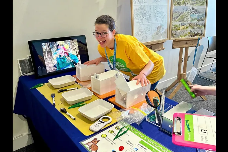 Pedersen of Alex wearing a yellow t-shirt standing behind a table full of props for Edinburgh Science festival