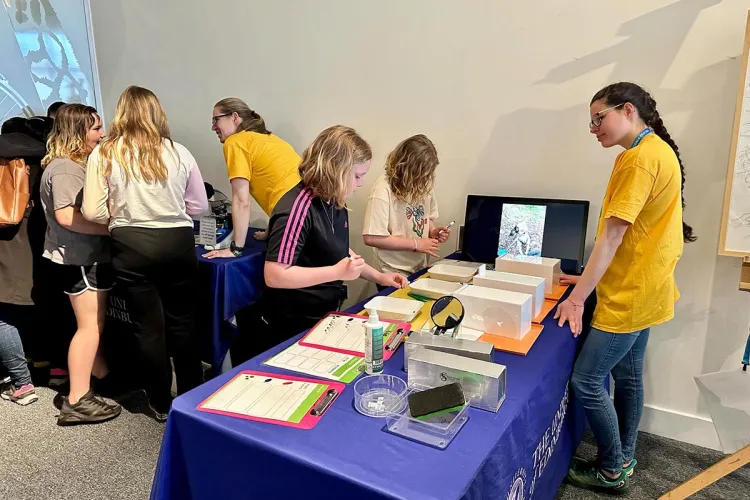 Photo of two group members in yellow t-shirts chatting with members of the public and showing them their props at the Edinburgh Science Festival 