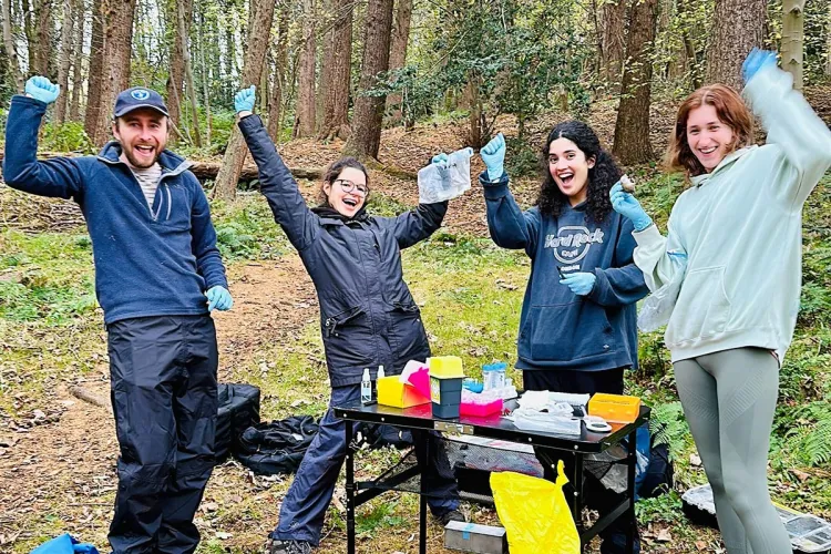 Photo of four fieldworkers standing in a celebratory pose in a wooded area with their samples