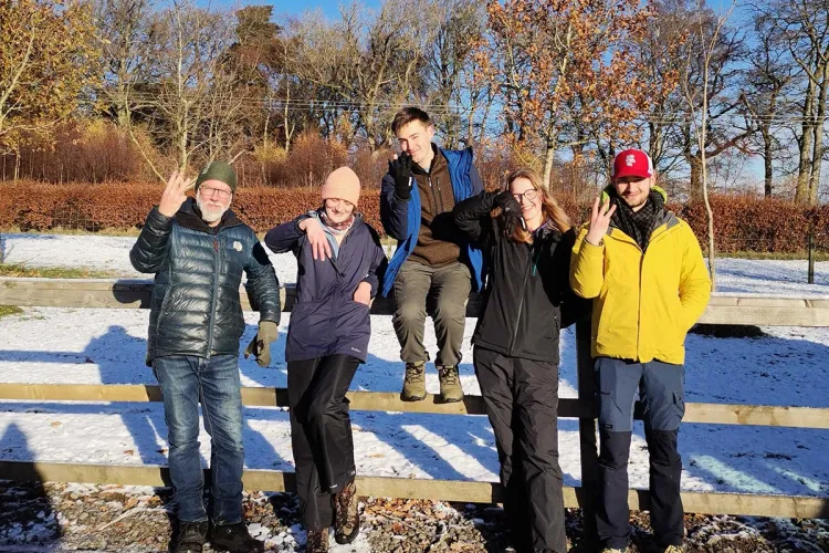 Photo of four fieldworkers standing in front of and sitting on a fence, the sun in their faces and a snowy field behind