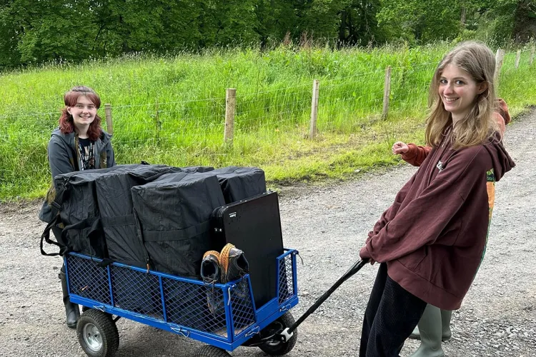 Photo of two fieldworkers one pushing, another pulling, a large cart on a gravely road near a fenced off grassy area