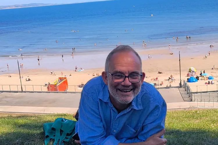 Kevin smiling while sitting in the grass at Lyme Regis