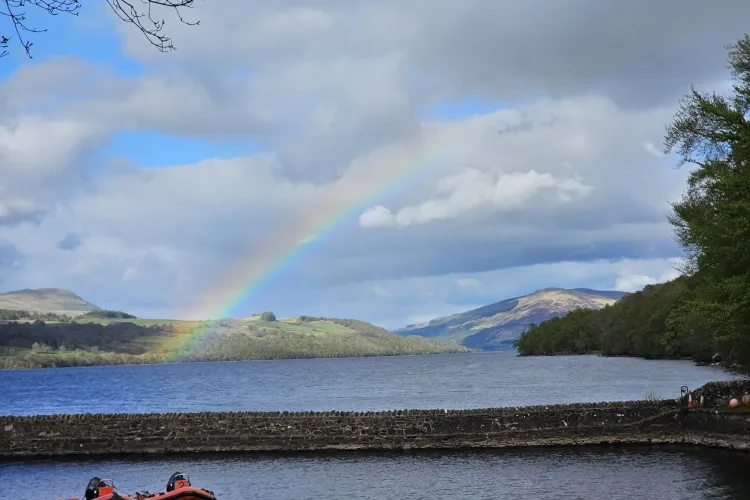 Image of a rainbow over Loch Tay, 2 speedboats sit in the harbour at the front of the image