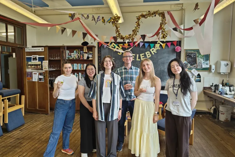 Photograph of six people standing in a decorated room with banners and streamers celebrating an event. 