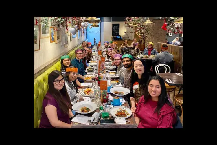 Photo of the lab group sitting round a table in a restaurant with plates of food, some wearing paper crowns