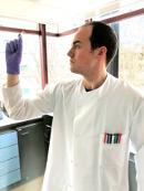 Dr(c) Marcos Valenzuela Ortega in the lab looking at a test tube.