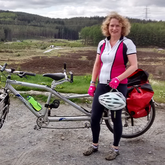 Julia Richardson standing near her bike with the view of hills behind.
