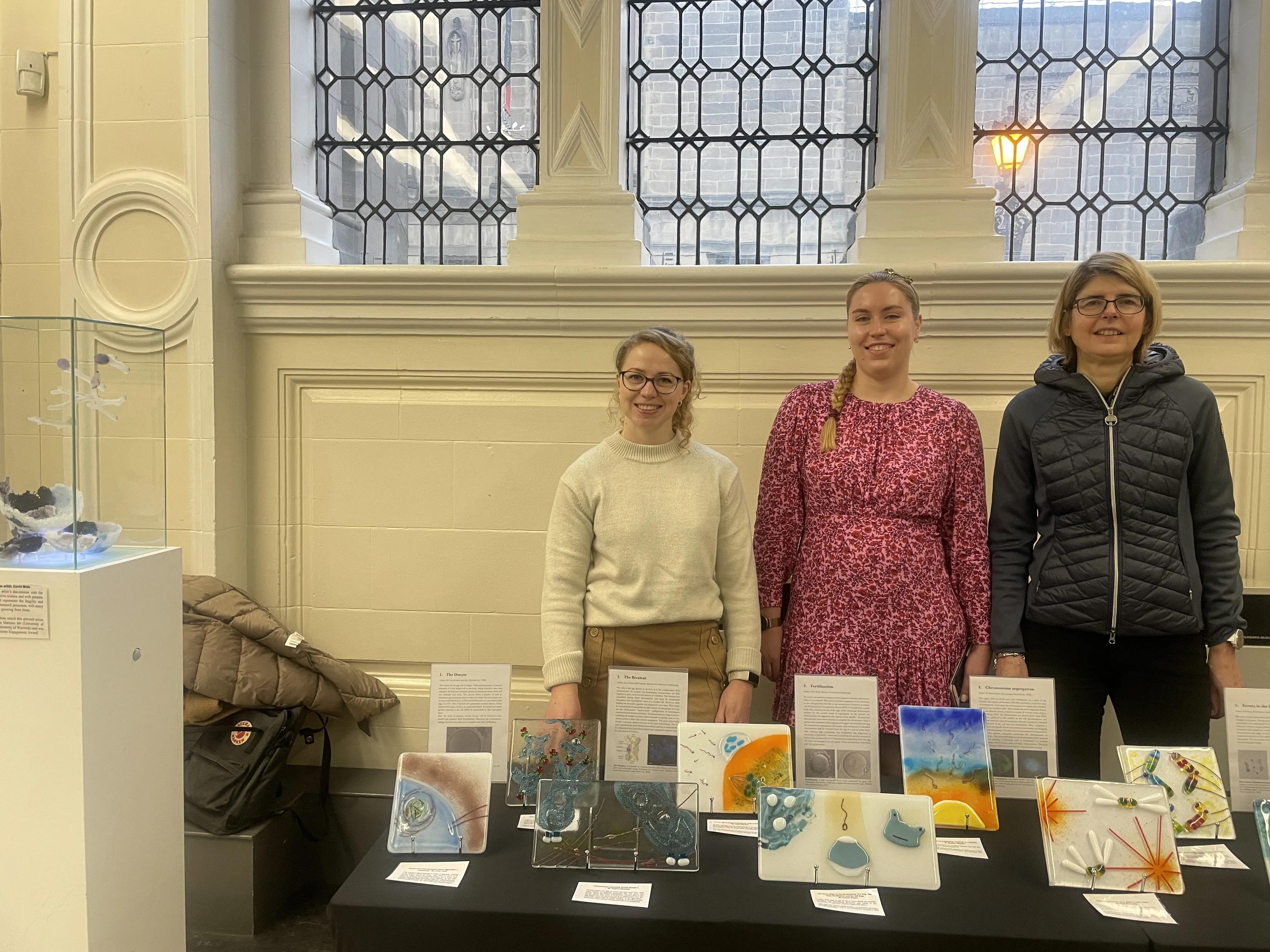 Three contributing artists posing at the exhibition stand with the tile artworks.