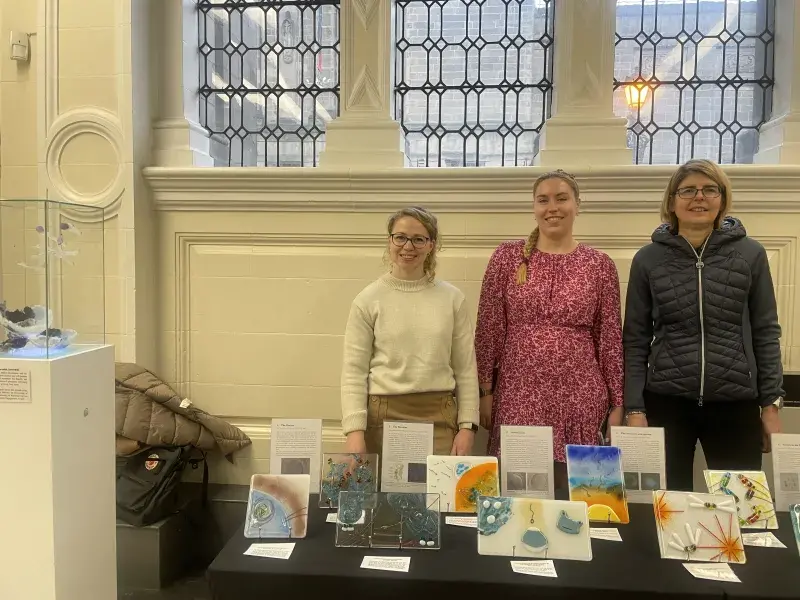 Three contributing artists posing at the exhibition stand with the tile artworks.
