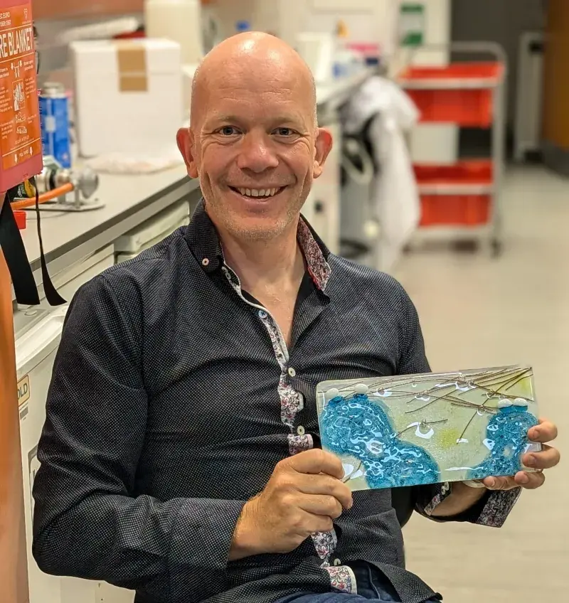 Andrew McAinsh posing with his tile artwork "Bivalents intertwined" in his lab.