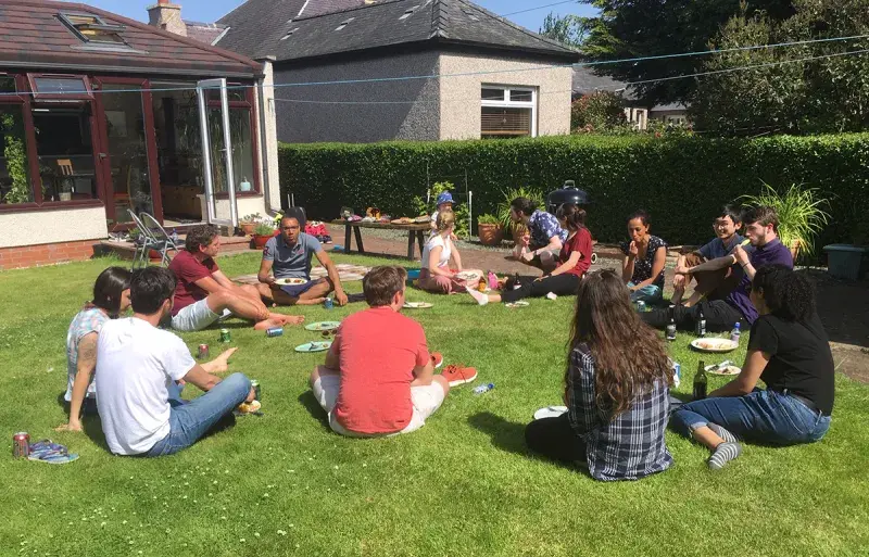 Philip group and Spoel group sitting on grass outside on a barbecue.
