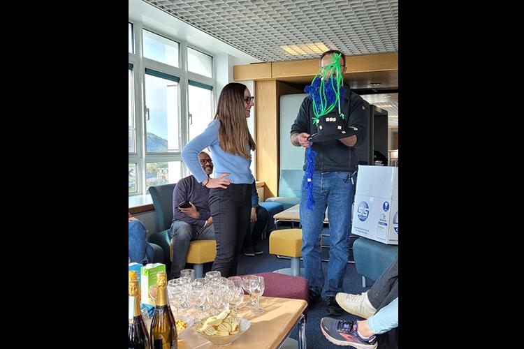 Lorenza is presented with a black hat decorated in green and blue cell structure at viva celebration