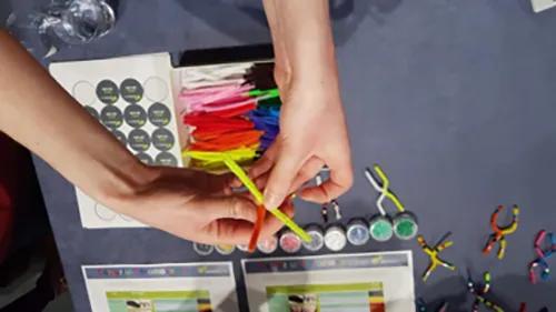 Hands hold colourful pipe cleaners over a table with craft supplies.