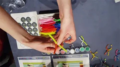 Hands hold colourful pipe cleaners over a table with craft supplies.