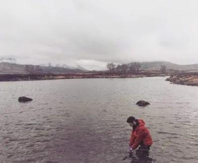A lab group member in a red jacket wades in a river to collect sample.