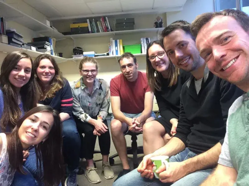 Photo of the lab group members seated in an office gathered together for a group photo