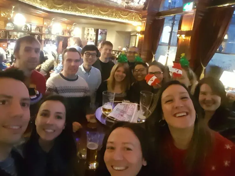 Photo of the lab group members in a pub, gathered for a group photo, they smile and many have Christmas hats