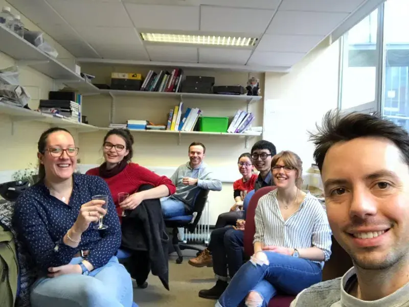 Lab group members in an office sitting, smiling for the camera with drinks