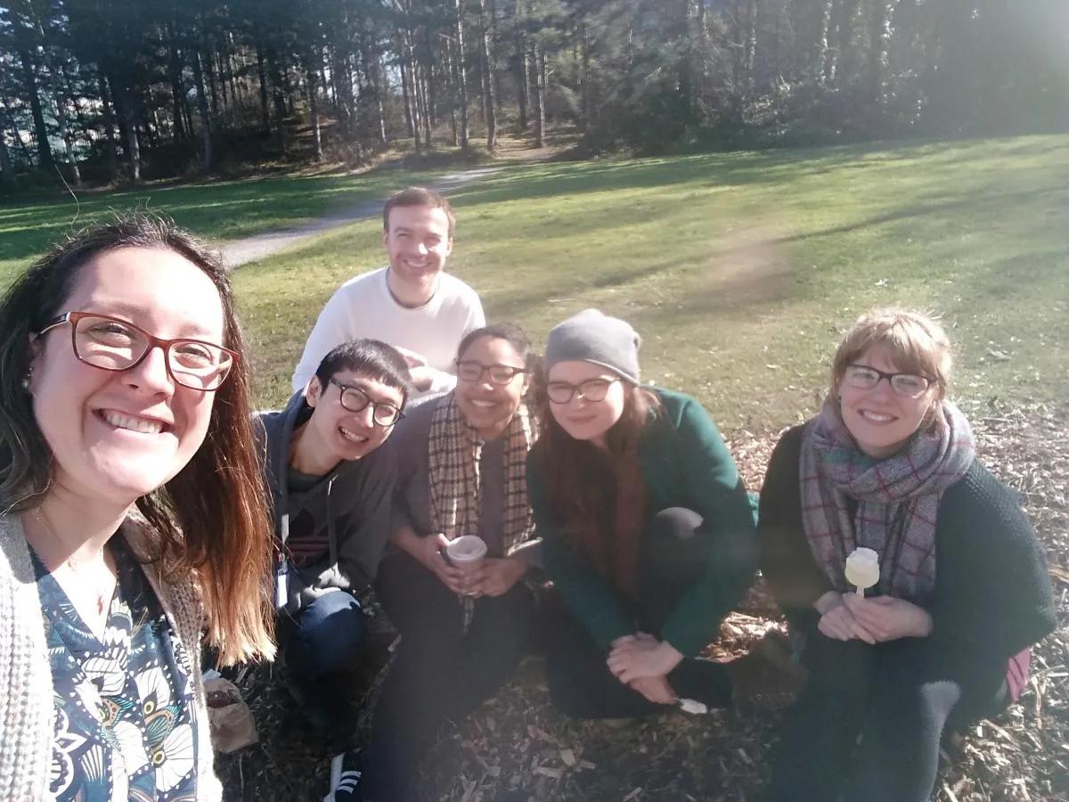 Lab group members pose for a photo crouched outside on grass, in front of trees