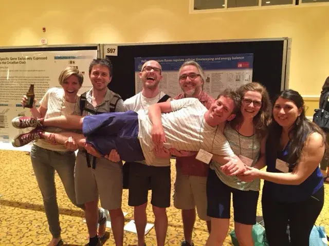 Gerben being held up horizontally by a group of people in front of research posters