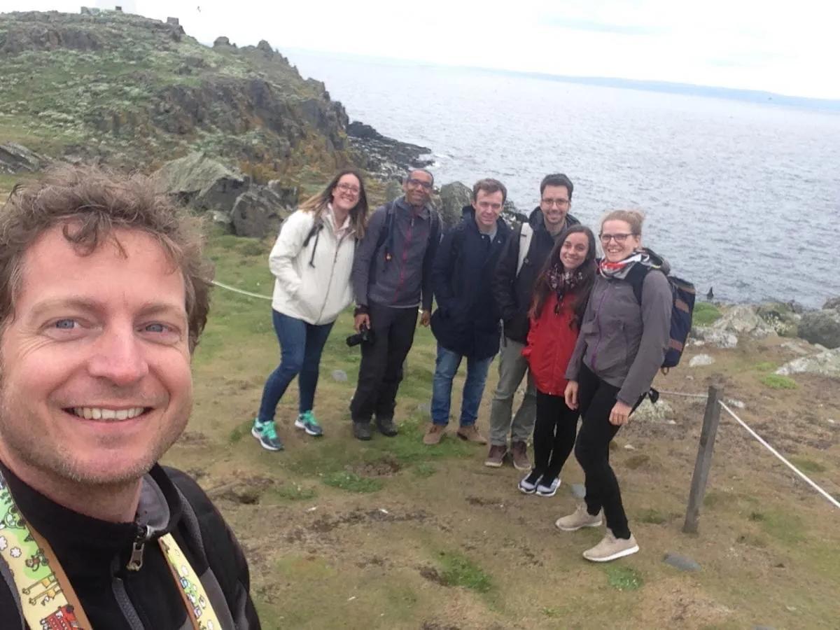Image of the lab group standing on grass in front of cliffs and rocks