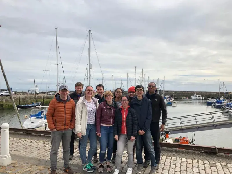 Lab group members pose for a photo in front of boats in a harbour