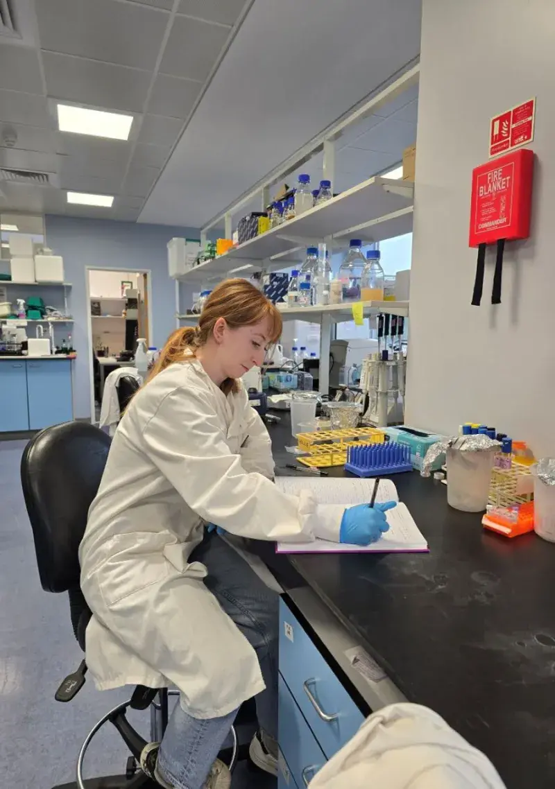 Photo of a student in the lab, wearing lab coat and gloves, using a microscope