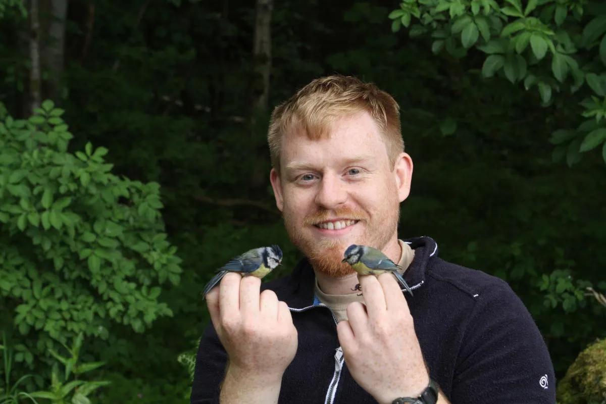 Photo of Shutt holding two blue tits. 