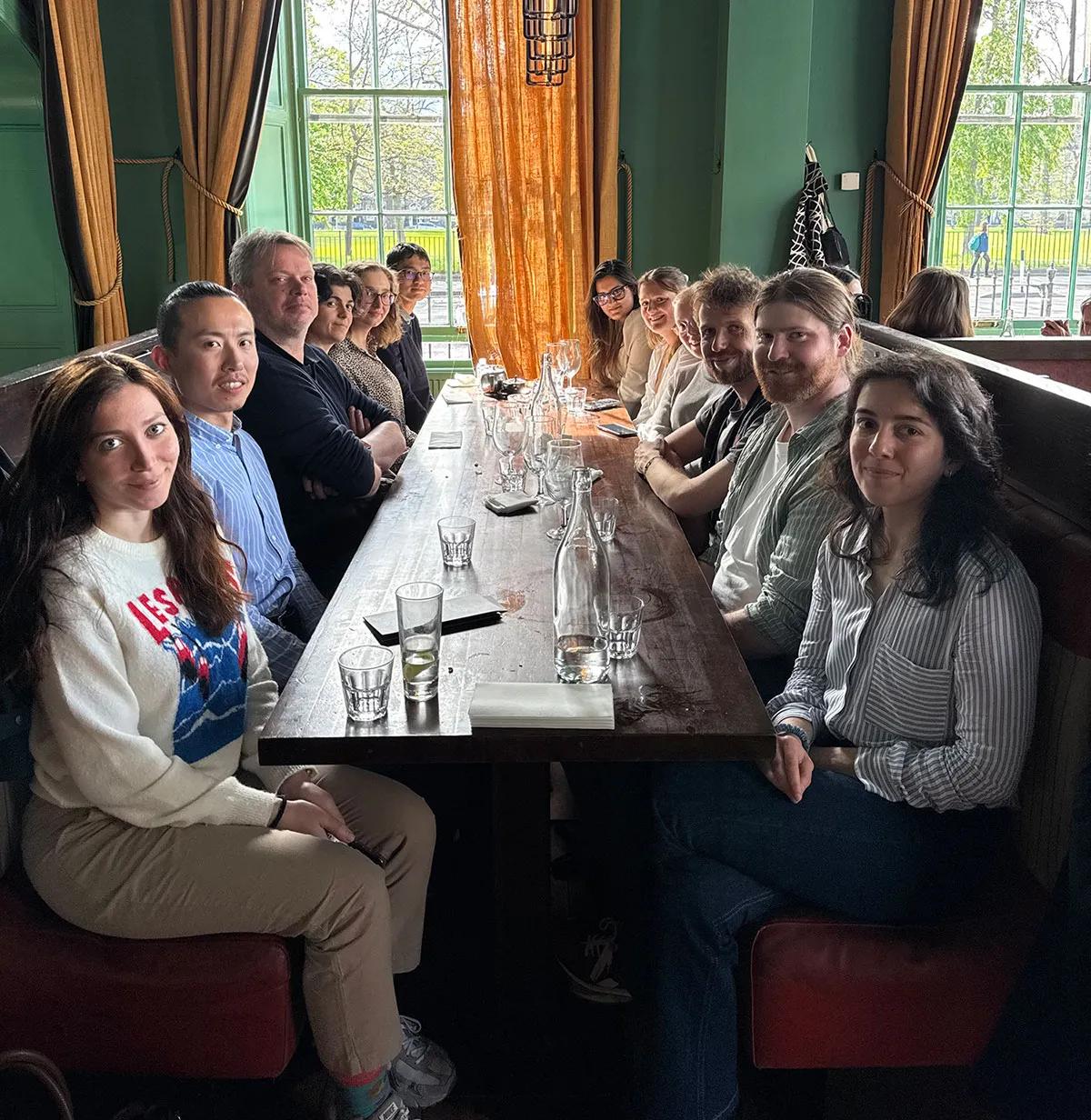 Photo of the lab group members sitting at a table in a restaurant with large windows off to the side.