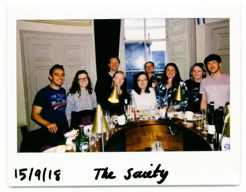 Photo of the lab group members posing for a photo whilst standing around a circular bar at the Scottish Malt Whisky Society