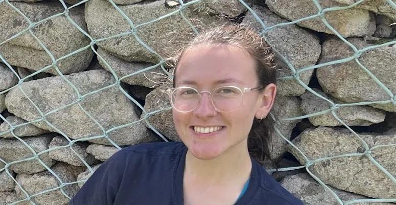 A woman looks at the camera smiling. She has glasses and her hair is up.