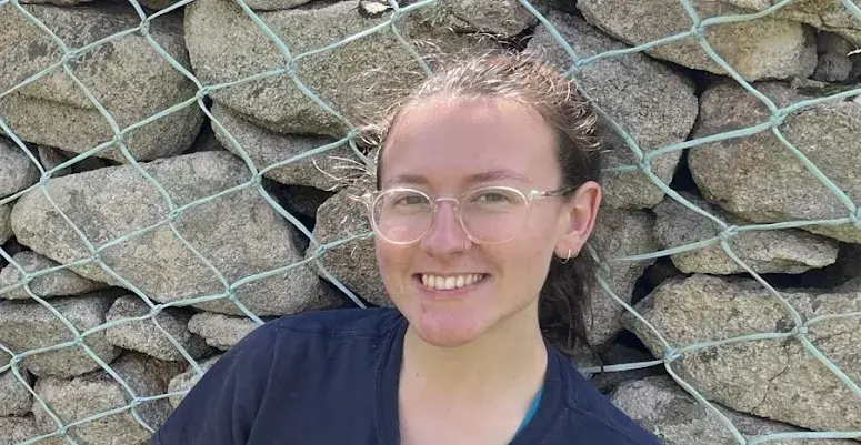 A woman looks at the camera smiling. She has glasses and her hair is up.
