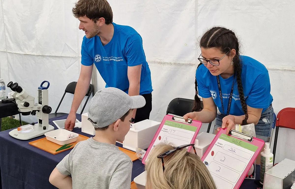 Two group members wearing blue t shirts chat to kids, represent Pedersen lab at the Falkirk Science Festival