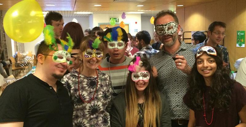 Lab group members, wearing carnival masks, pose for photo