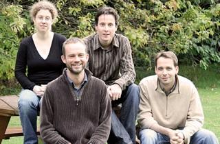 Four lab group sit outside on a bench and pose for photo