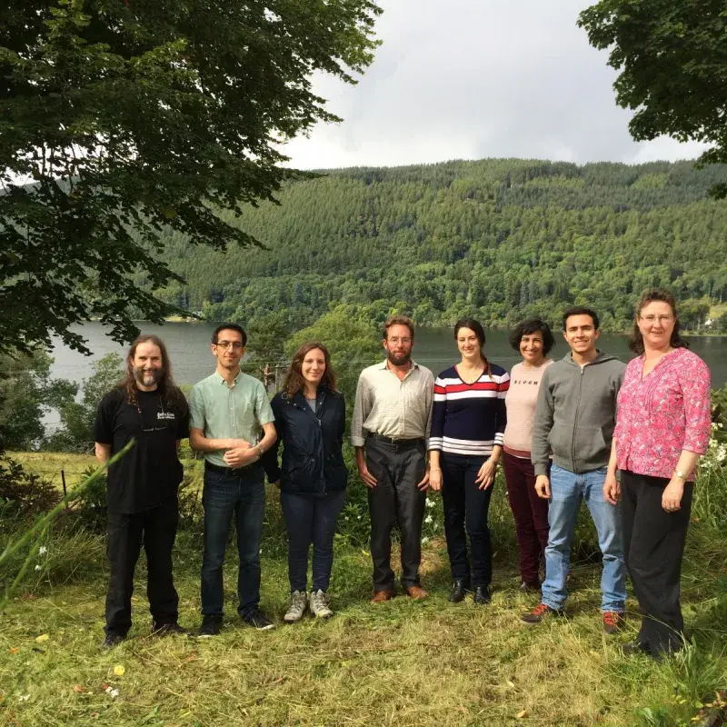 Group members pose for a photo in front of a lake surrounded by trees