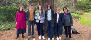 Group photo of the six lab members in a forest in front of a tree