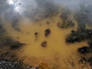 Photo of a riverbed with yellowish brown sediment and patches of green algae