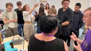 Photo of students gathered for a workshop, standing and chatting about their work