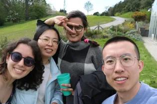 Selfie of 4 lab group members standing in a green space, smiling for the camera