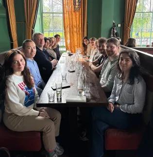 Photo of the lab group members sitting at a table in a restaurant with large windows off to the side.