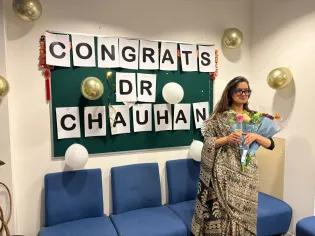 Photo of Mehak holding bunches of flowers in front of a noticeboard with "Congrats Dr Chauhan" printed out on pieces of paper 