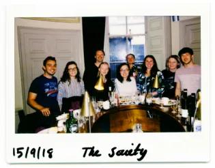 Photo of the lab group members posing for a photo whilst standing around a circular bar at the Scottish Malt Whisky Society