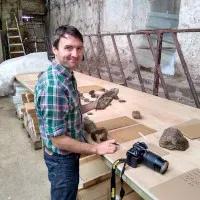 Dr Sandy Hetherington stands in front of a table holding a fossil in his left hand