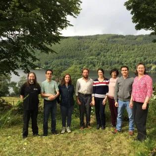 Group members pose for a photo in front of a lake surrounded by trees