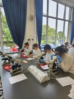 Students in a lab wearing white coats working at benches 