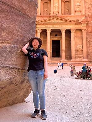 Photo of Qingqin standing in front of a temple carved into a cave