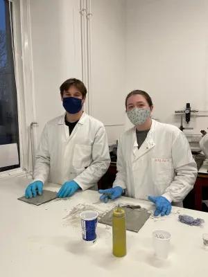 Two students stand in lab coats and masks preparing peels